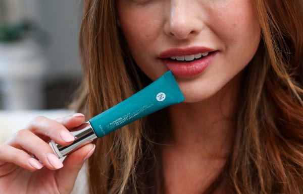 A woman holding the Lip Plumping Serum up to her lips.
